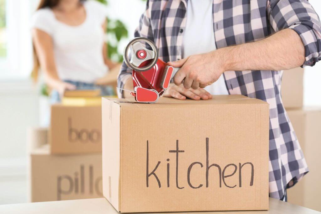 A man at home taping a package that has a label for kitchen things