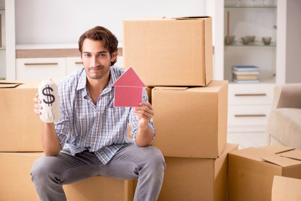 A man holding money and a paper house while packing for long-distance moving