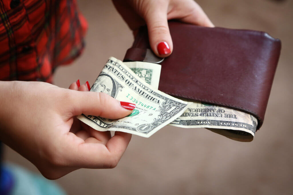 A woman holding a wallet and a dollar bill while going to the bank
