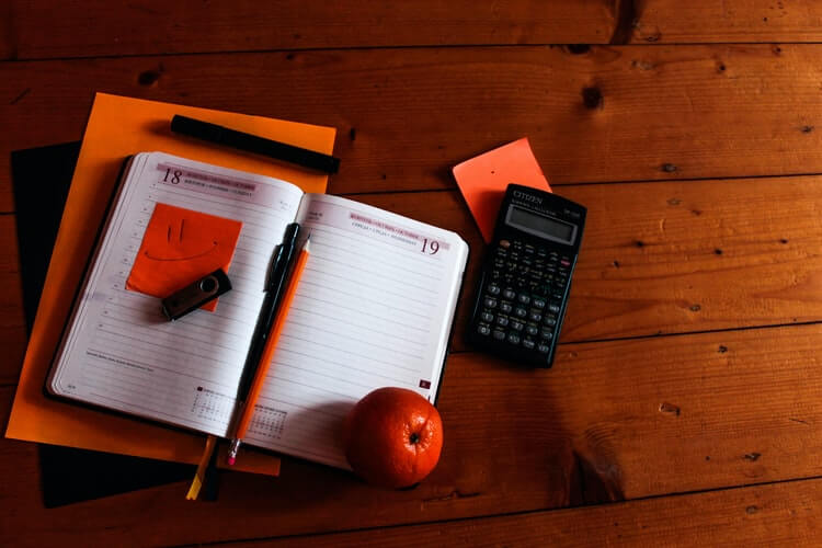 Black calculator, notebook, and orange on a table