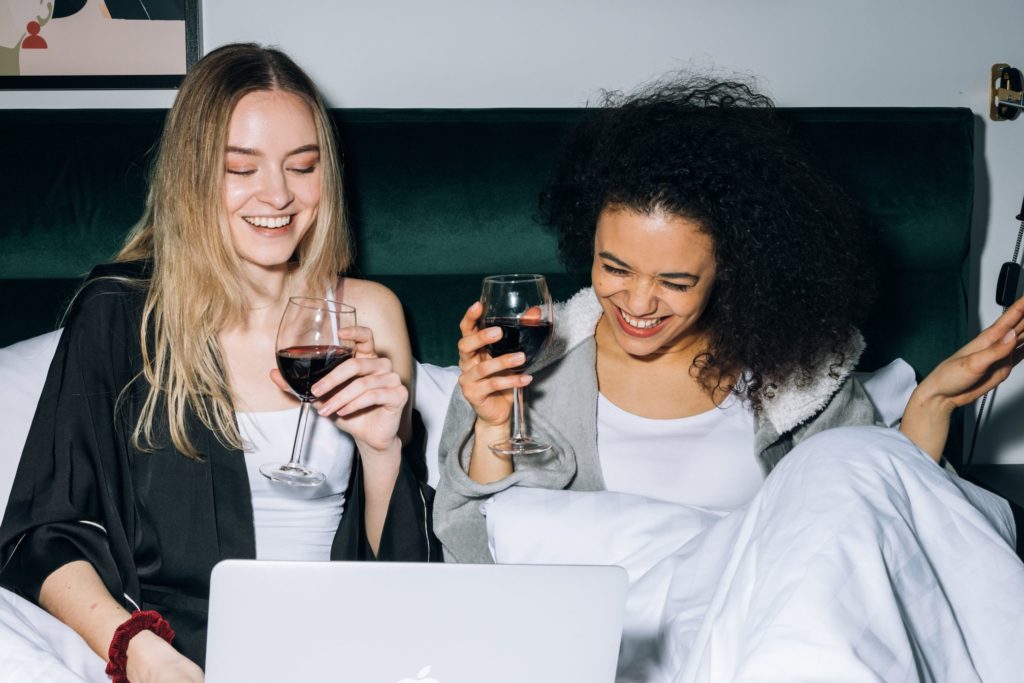 Two girls drinking wine and smiling after long-distance moving