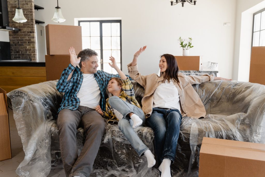 family sitting on a still wrapped couch after a long-distance moving