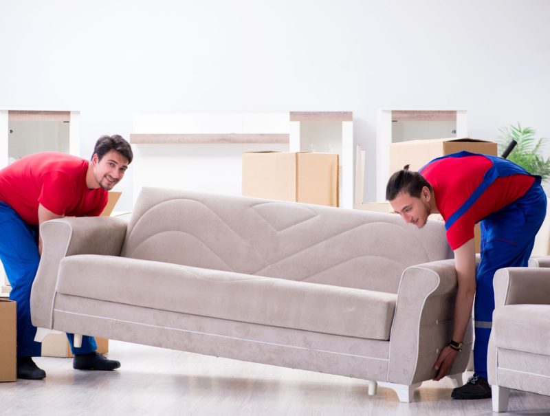 Two professional cross-country movers lifting a heavy couch