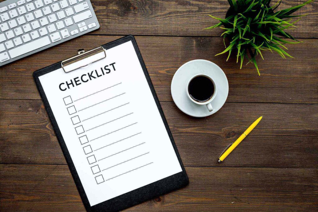 A clipboard with paper that says checklist on a table with some coffee