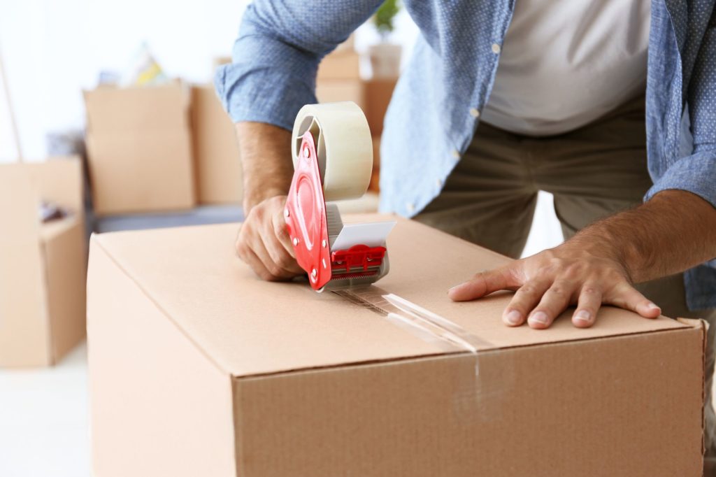 a man using a duct tape dispenser to seal a box for cross-country moving