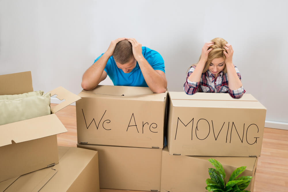 two frustrated people leaning onto boxes in the middle of moving long distance