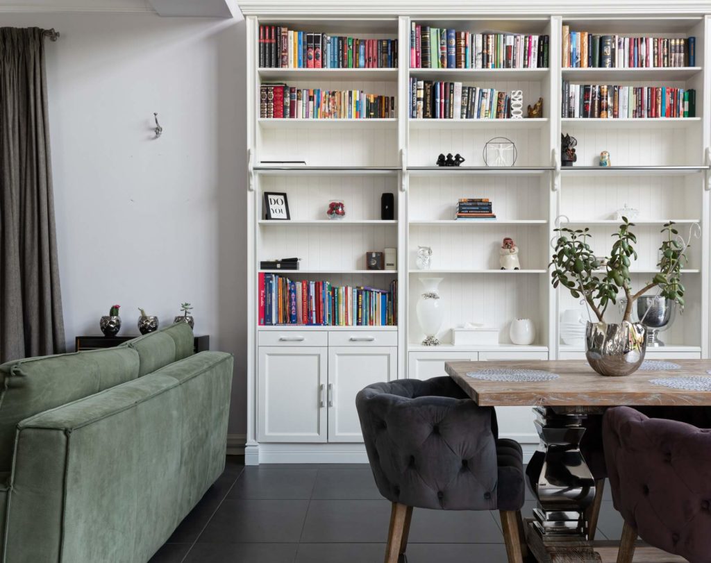 a white, semi-full bookshelf next to a dining table with a plant on