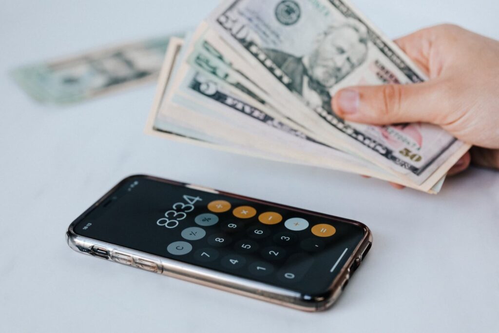 A hand holding cash beside a calculator