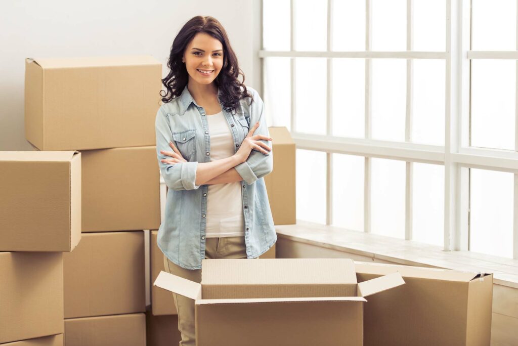 A woman surrounded by boxes, smiling into the camera
